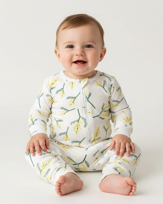 Design a vibrant, studio photoshoot scene capturing a gorgeous 9 month old boy wearing the ''Full bodysuit in wattle print' and looking at the camera with an innocent, sweet face. The backdrop is off-white and the camera should be angled slightly downward