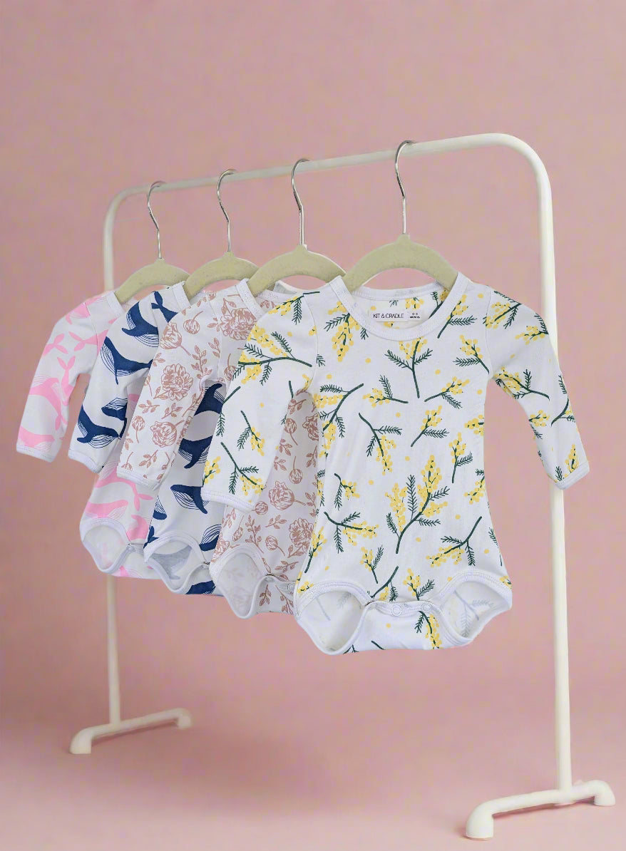 Set of baby bodysuits with floral patterns hanging on a rack against a white background
